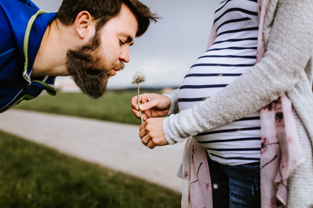 Mann pustet Pusteblume vor Babybauch