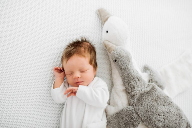 Baby schläft mit Kuscheltiere auf weißer Strickdecke