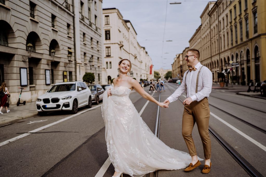 Braut und Bräutigam laufen über die Straßenbahnschiene in München