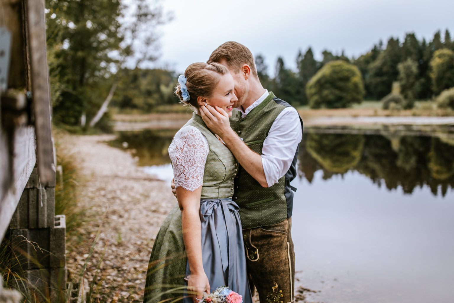 Bräutigam küsst seine Frau am See in Tracht in der Nähe von Weilheim