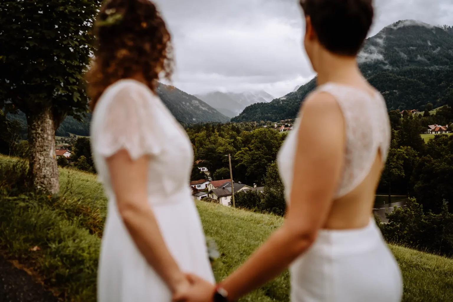 Beide Bräute schauen bei vor der freien Trauung in die Ferne in die wolkenverhangenen Berge der Alpen